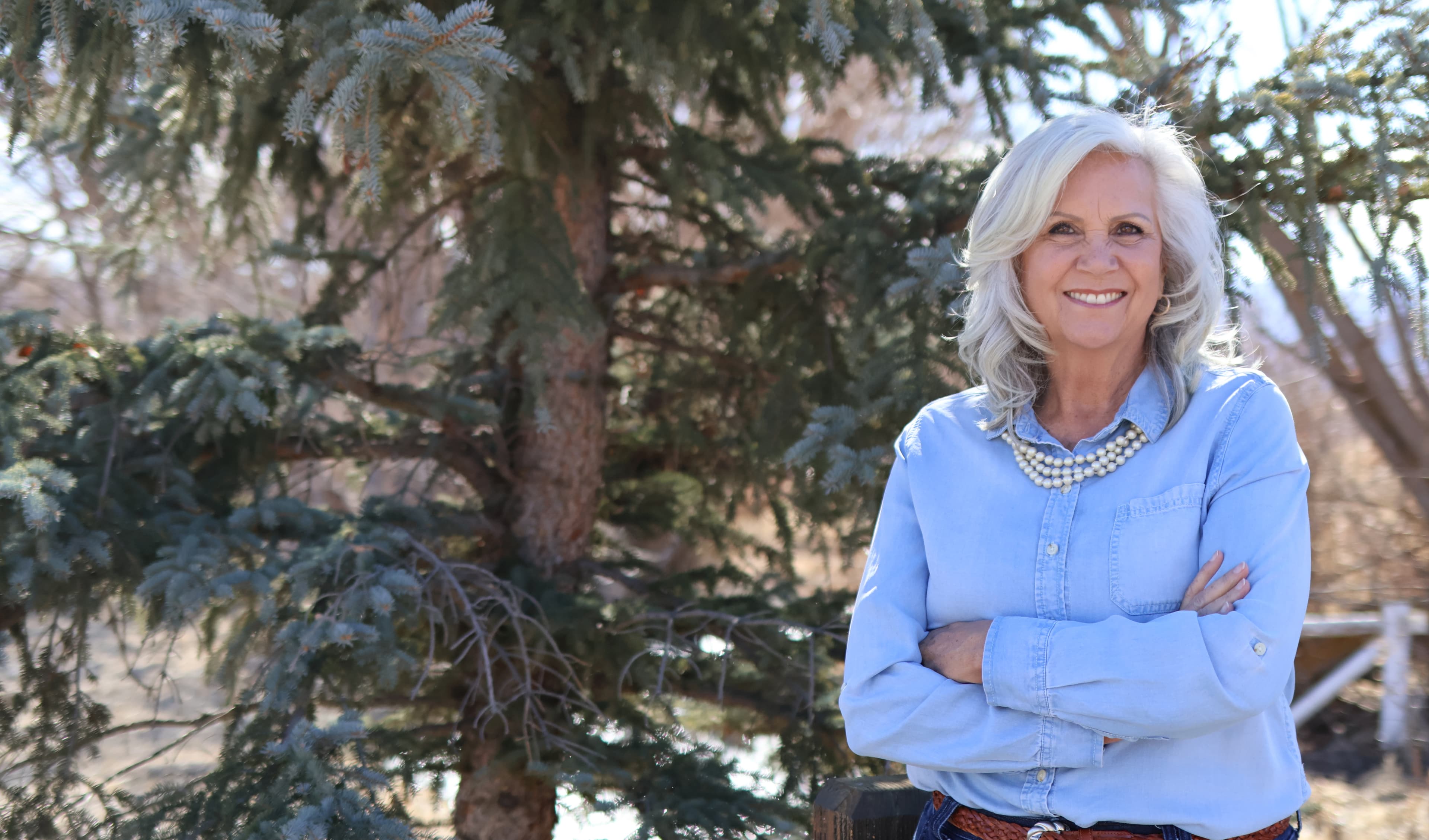 Celeste Johnson smiling outdoors beside an evergreen tree in the Wasatch Back