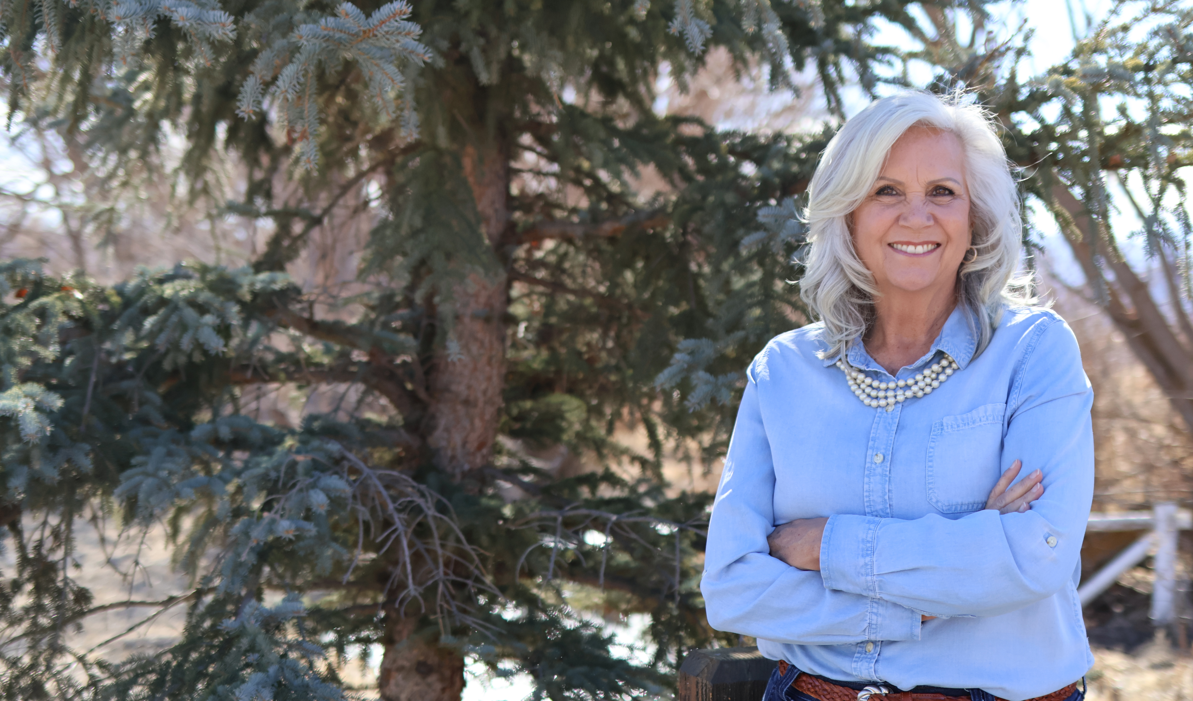 Celeste Johnson smiling outdoors beside an evergreen tree in the Wasatch Back